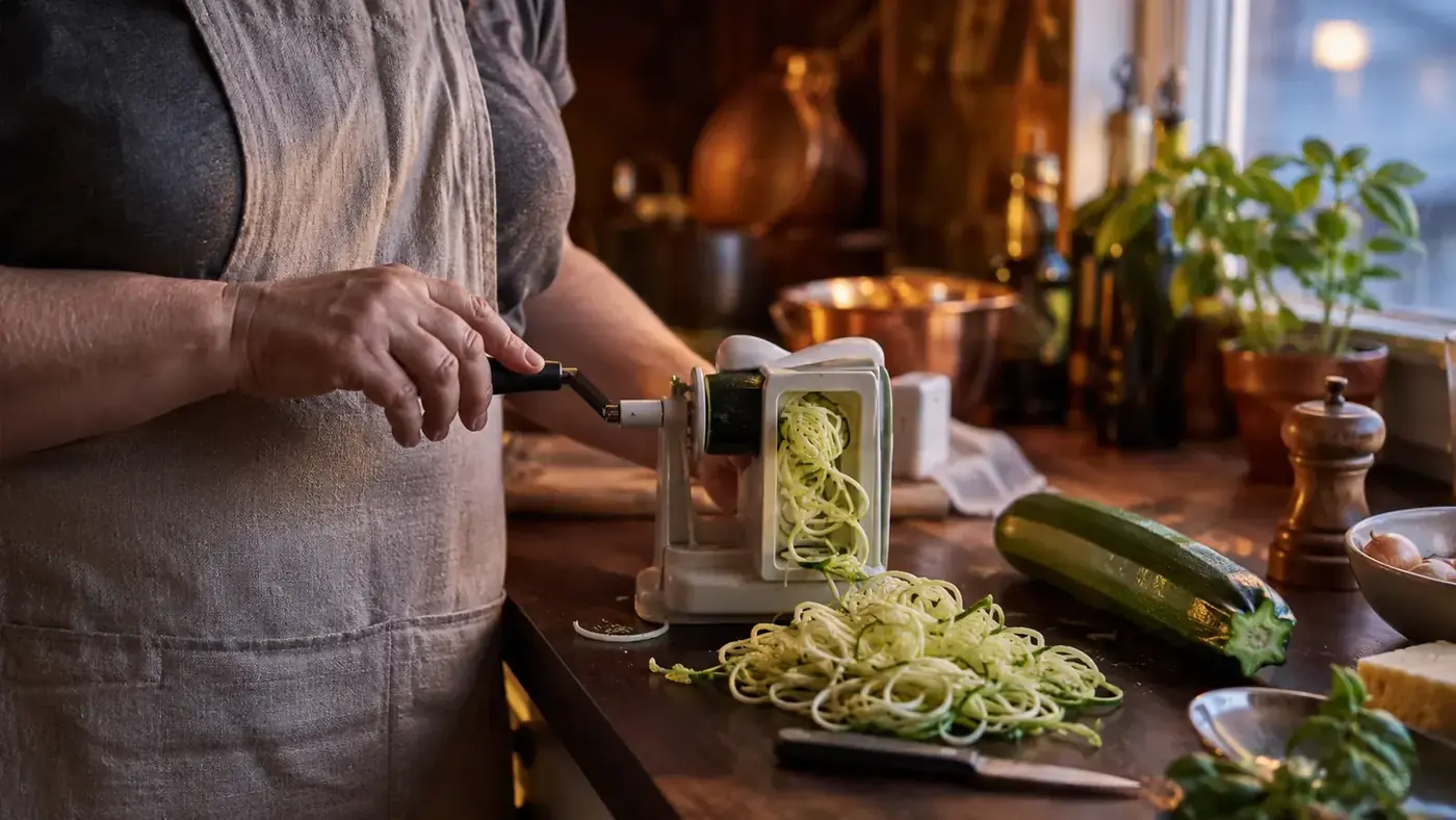 A pile of curly zucchini noodles next to a spiralizer on a wooden kitchen counter