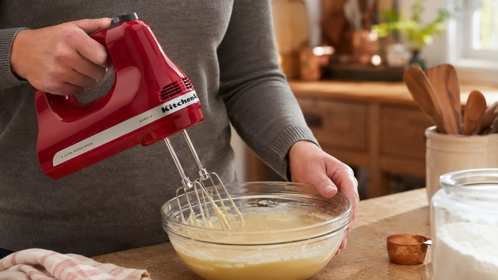 Hand holding a KitchenAid hand mixer lifting beaters out of cake batter