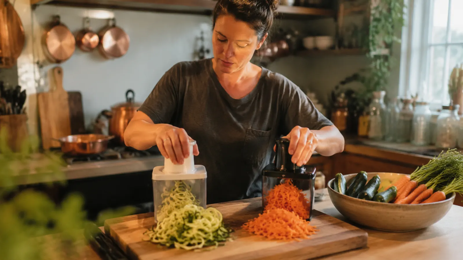 A Brieftons vegetable spiralizer and a mandoline slicer sitting side by side on a kitchen counter with fresh zucchini and carrots